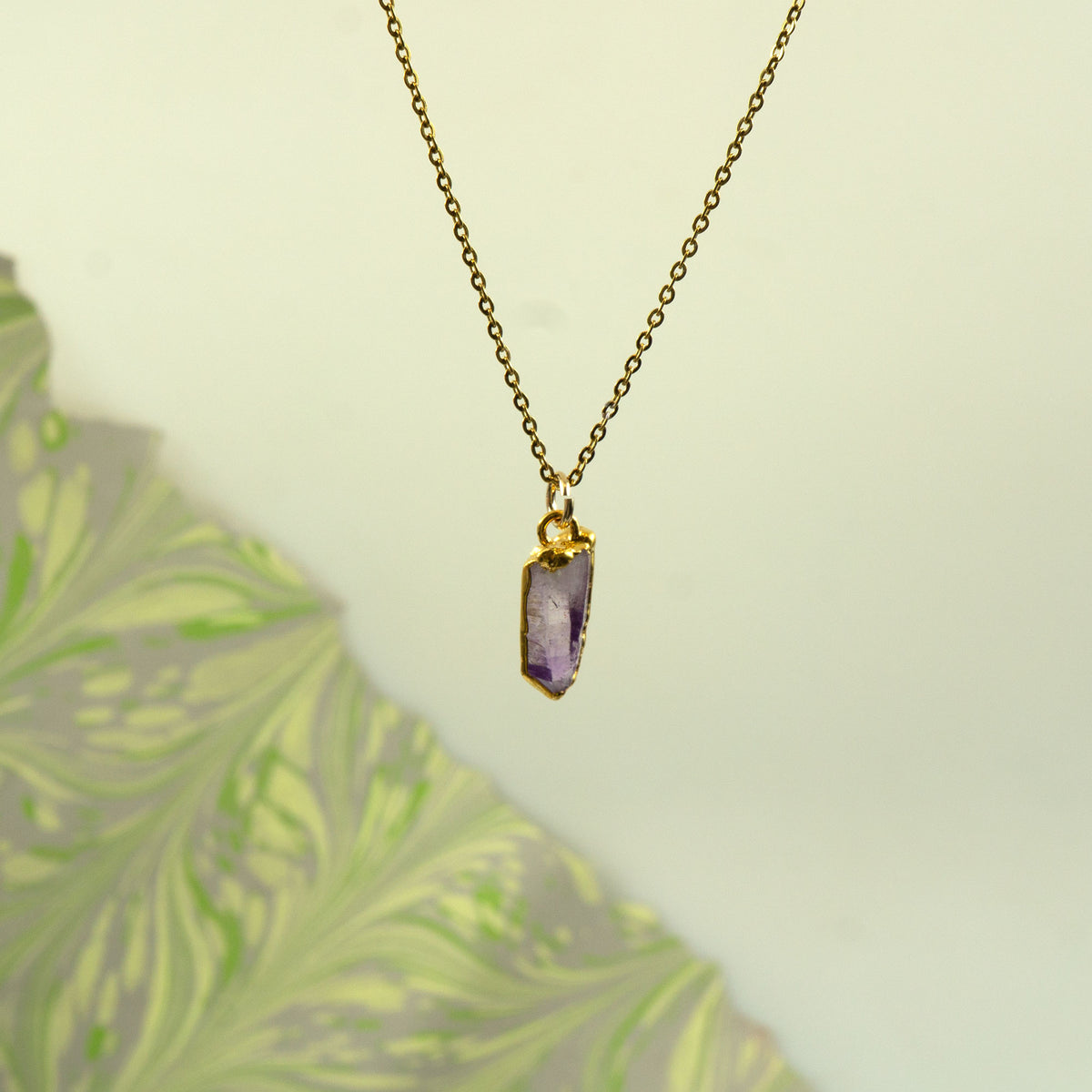 A gold chain necklace with a raw, faceted purple amethyst crystal pendant