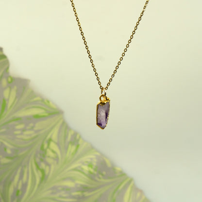 A gold chain necklace with a raw, faceted purple amethyst crystal pendant