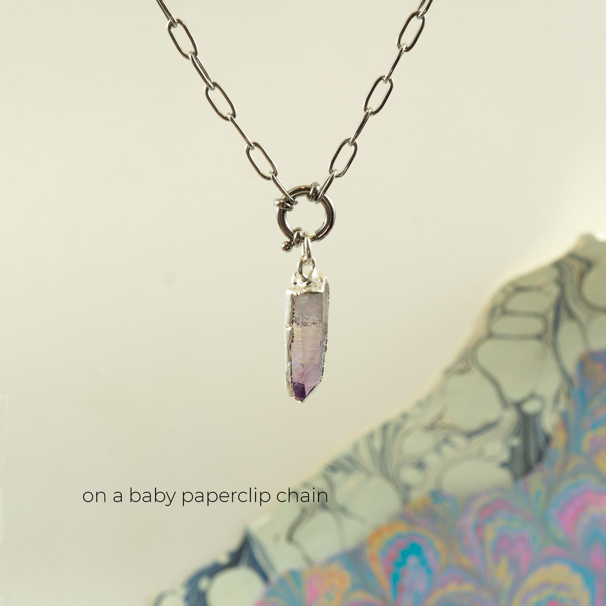 A silver baby paperclip chain necklace with a small ring clasp holding a tapered purple amethyst crystal pendant