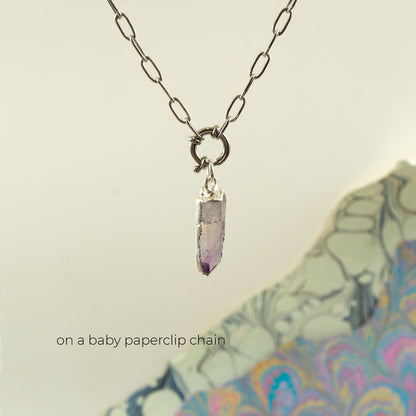 A silver baby paperclip chain necklace with a small ring clasp holding a tapered purple amethyst crystal pendant