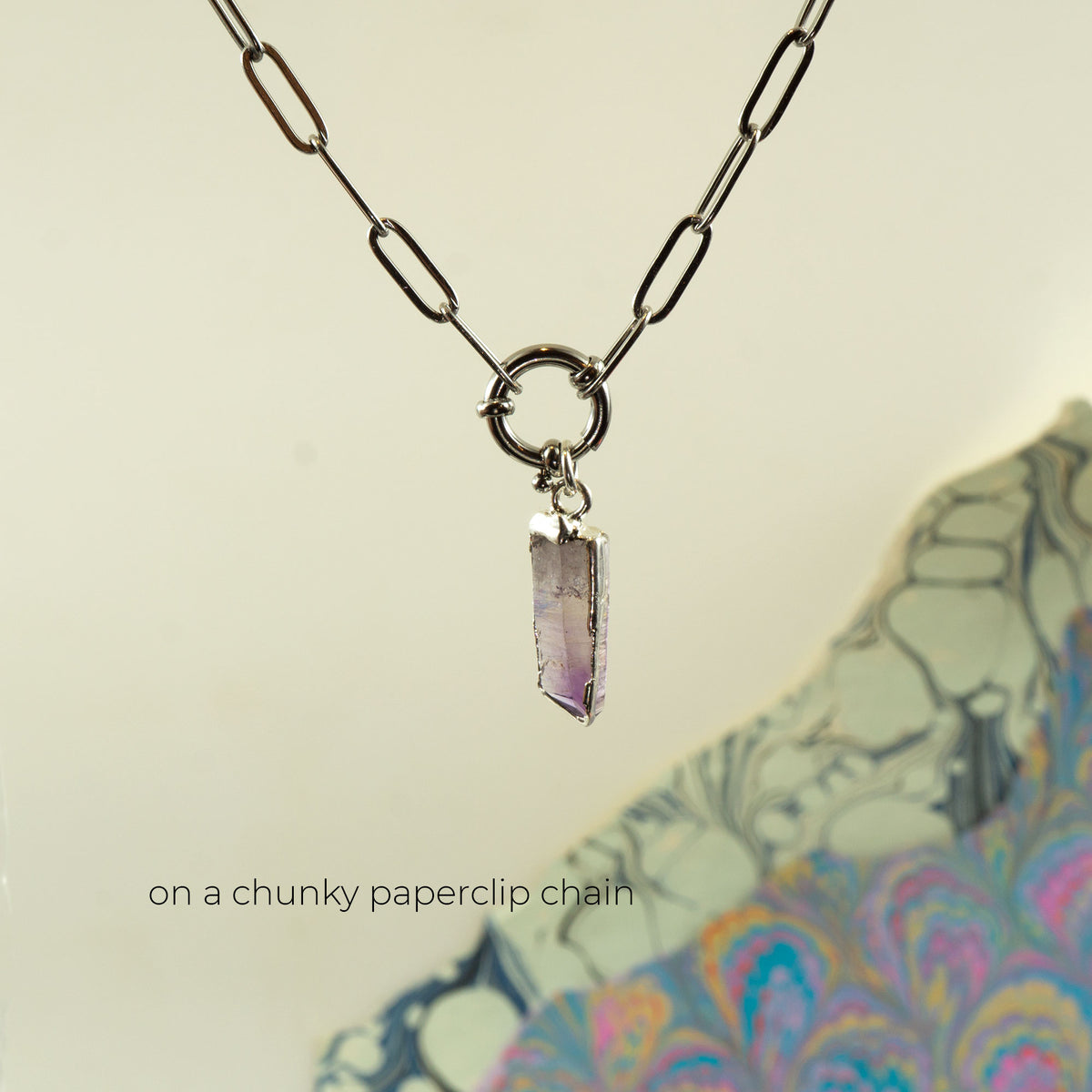 A silver chunky paperclip chain necklace with a dangling raw amethyst crystal point