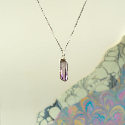 A silver chain necklace with a faceted purple amethyst crystal pendant