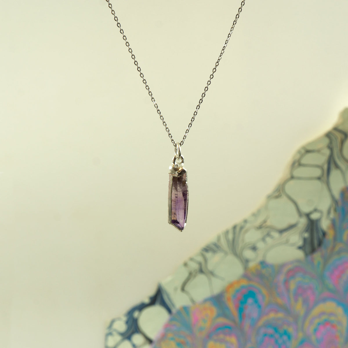A silver chain necklace with a raw, faceted purple amethyst crystal pendant.