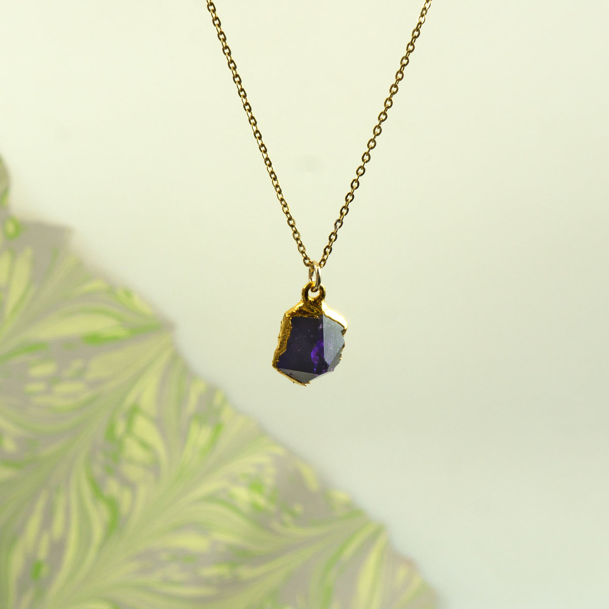 A gold chain necklace with a raw, irregular-cut purple Amethyst gemstone pendant