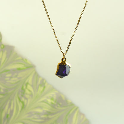 A gold chain necklace with a raw, irregular-cut purple Amethyst gemstone pendant