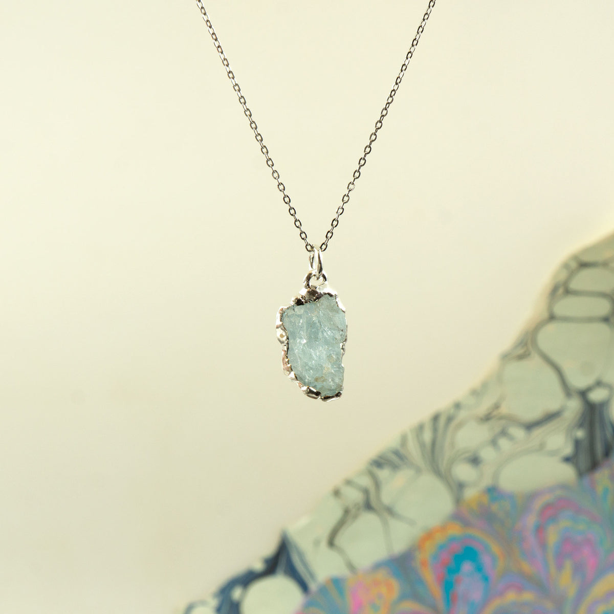 A silver chain necklace with a raw, polished light blue aquamarine gemstone pendant