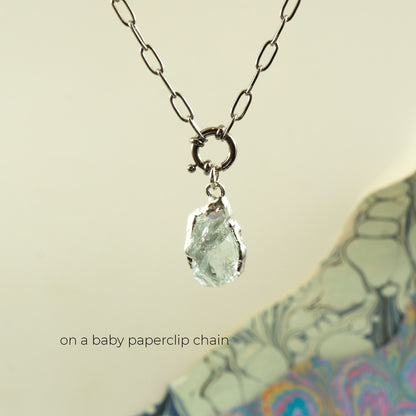 A silver paperclip chain necklace with a raw, faceted aquamarine gemstone pendant