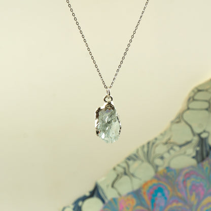 A silver chain necklace with a teardrop-shaped clear aquamarine gemstone pendant