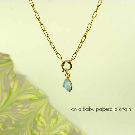 A gold paperclip chain necklace with a small gold clasp and a dangling light blue aquamarine teardrop gemstone