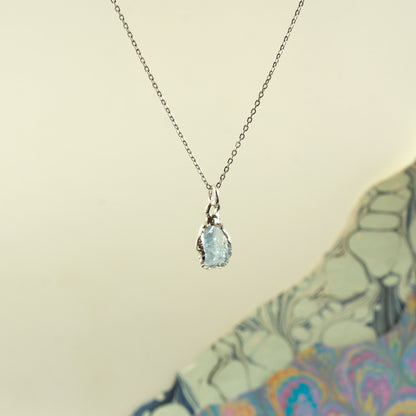 A silver chain necklace with a teardrop-shaped light blue aquamarine gemstone pendant