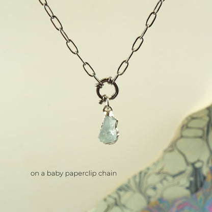 A silver paperclip chain necklace with a small ring clasp holding a raw, irregular aquamarine stone pendant
