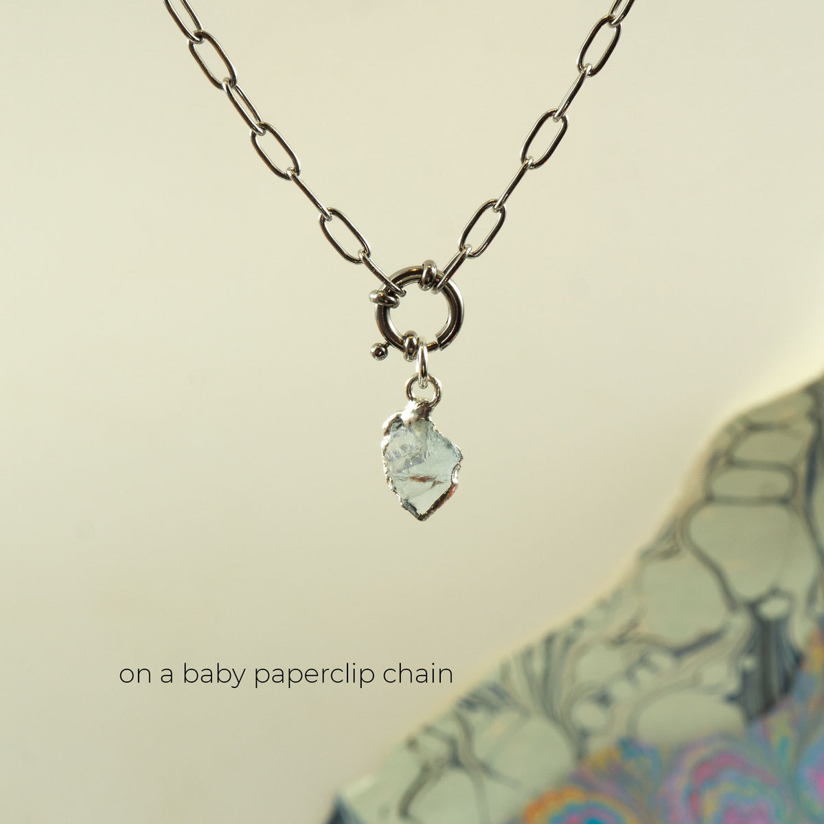 A silver paperclip chain necklace with a ring clasp and a small Aquamarine faceted gemstone pendant