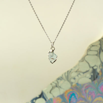 A silver chain necklace with a small, irregular-shaped Aquamarine gemstone pendant