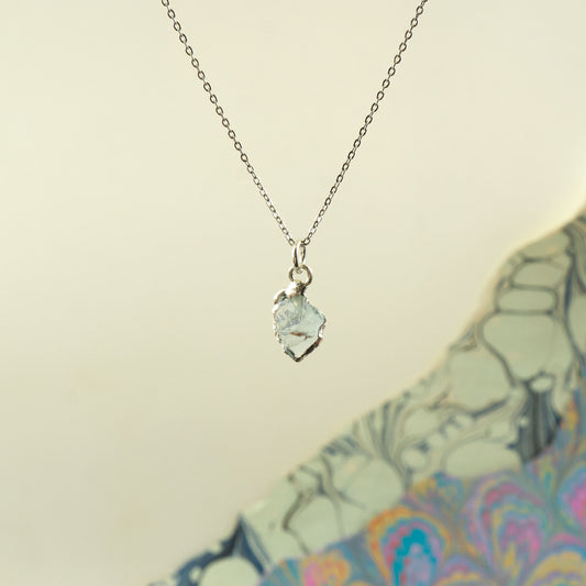 A silver chain necklace with a small, irregular-shaped Aquamarine gemstone pendant