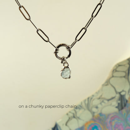 A silver paperclip chain necklace with a ring clasp and a small raw, irregular-cut light blue aquamarine gemstone charm