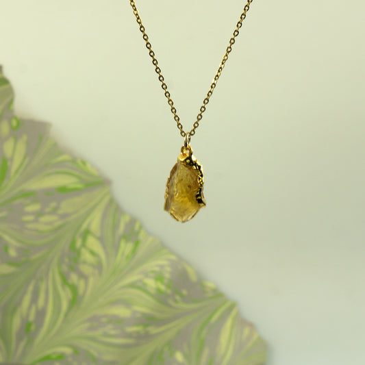 A gold chain necklace with a raw, yellow citrine pendant.