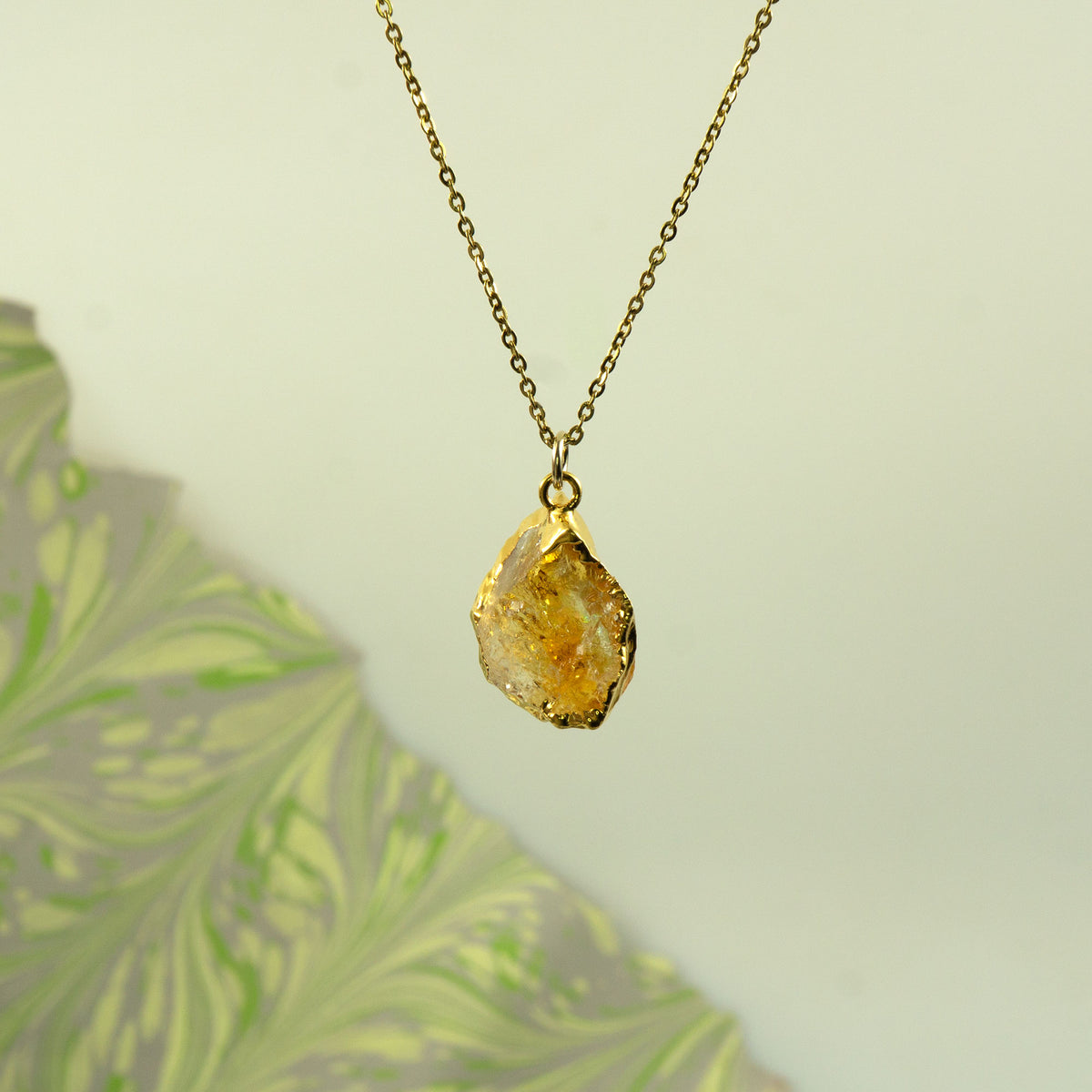 A gold chain necklace with a raw, irregular yellow citrine  gemstone pendant.