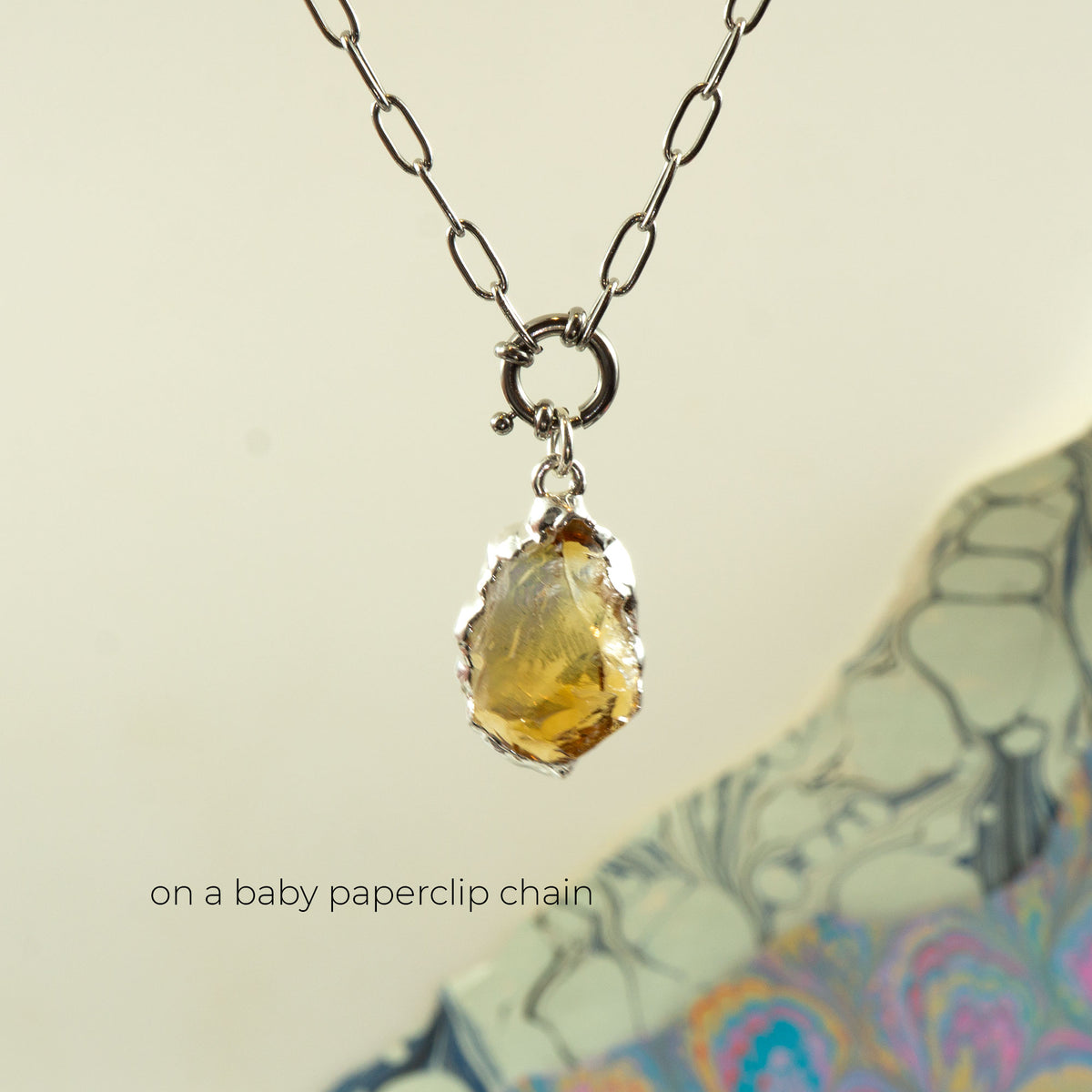 A silver paperclip chain necklace with a raw, irregular yellow citrine gemstone pendant.