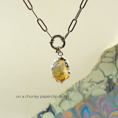 A silver paperclip chain necklace with a ring clasp holding a raw, irregular yellow citrine gemstone pendant