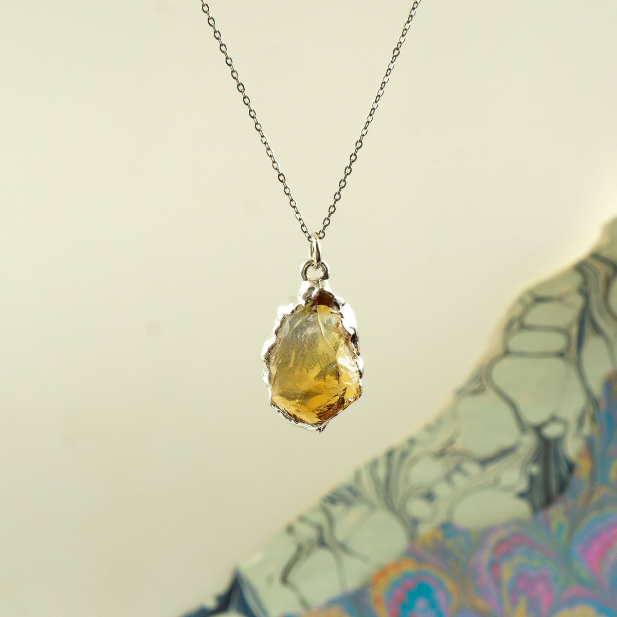 A silver chain necklace with a raw, irregular yellow citrine gemstone pendant, 