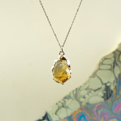 A silver chain necklace with a raw, irregular yellow citrine gemstone pendant, 