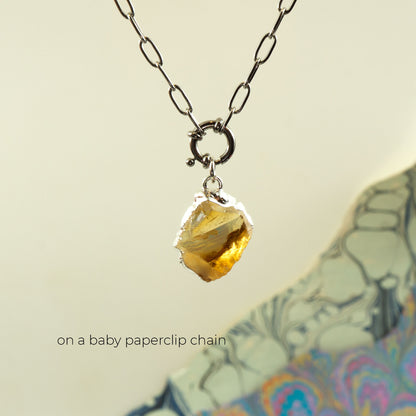 A silver paperclip chain necklace with a raw, yellow citrine gemstone pendant,
