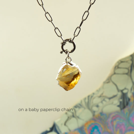 A silver paperclip chain necklace with a raw, yellow citrine gemstone pendant,