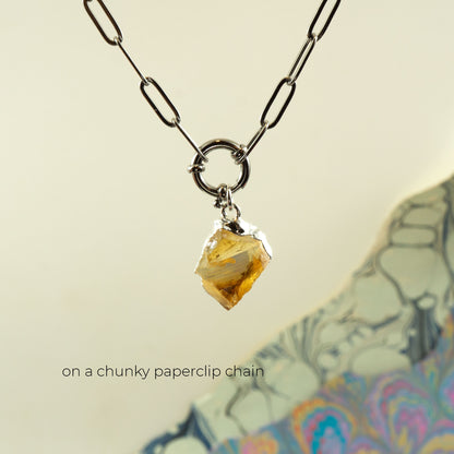 A raw yellow citrine gemstone pendant hanging from a chunky silver paperclip chain necklace.