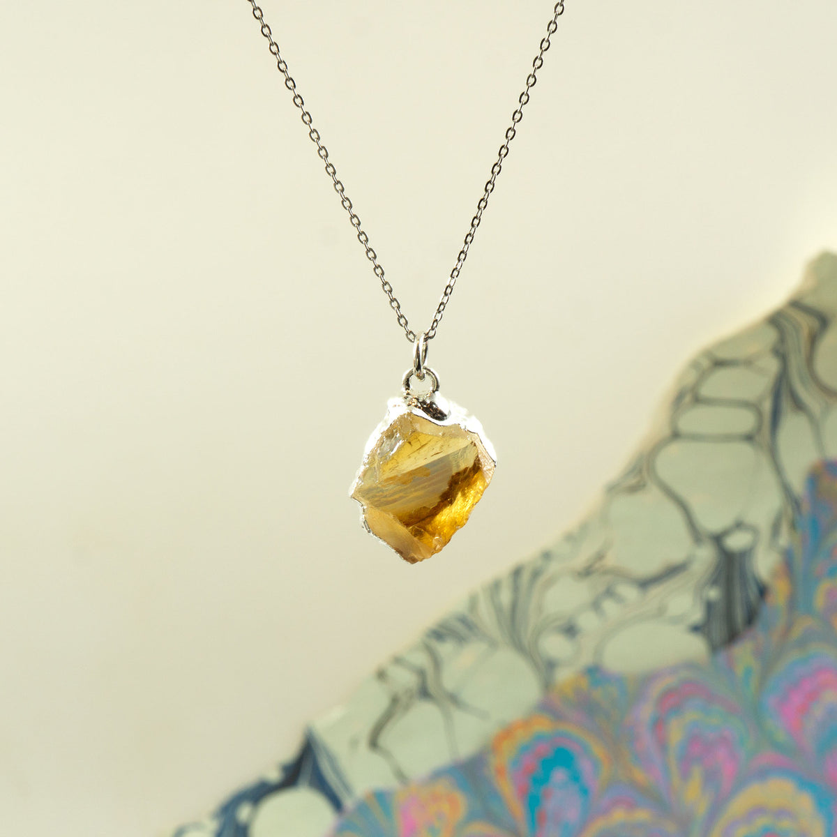 A silver chain necklace with a raw, irregular yellow citrine gemstone pendant.