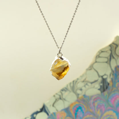 A silver chain necklace with a raw, irregular yellow citrine gemstone pendant.