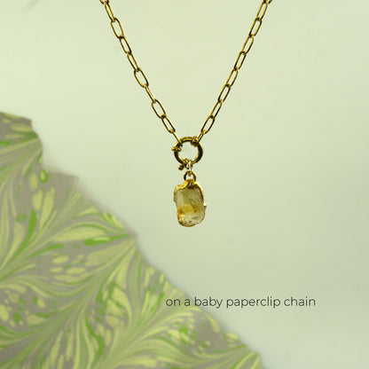 A gold paperclip chain necklace with a small raw, bezel-set yellow citrine stone pendant