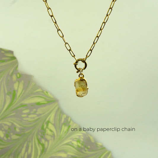 A gold paperclip chain necklace with a small raw, bezel-set yellow citrine stone pendant