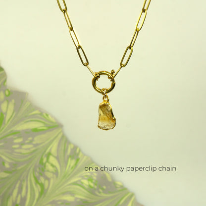A gold paperclip chain necklace with a ring clasp and a raw, irregular amber-yellow stone citrine pendant
