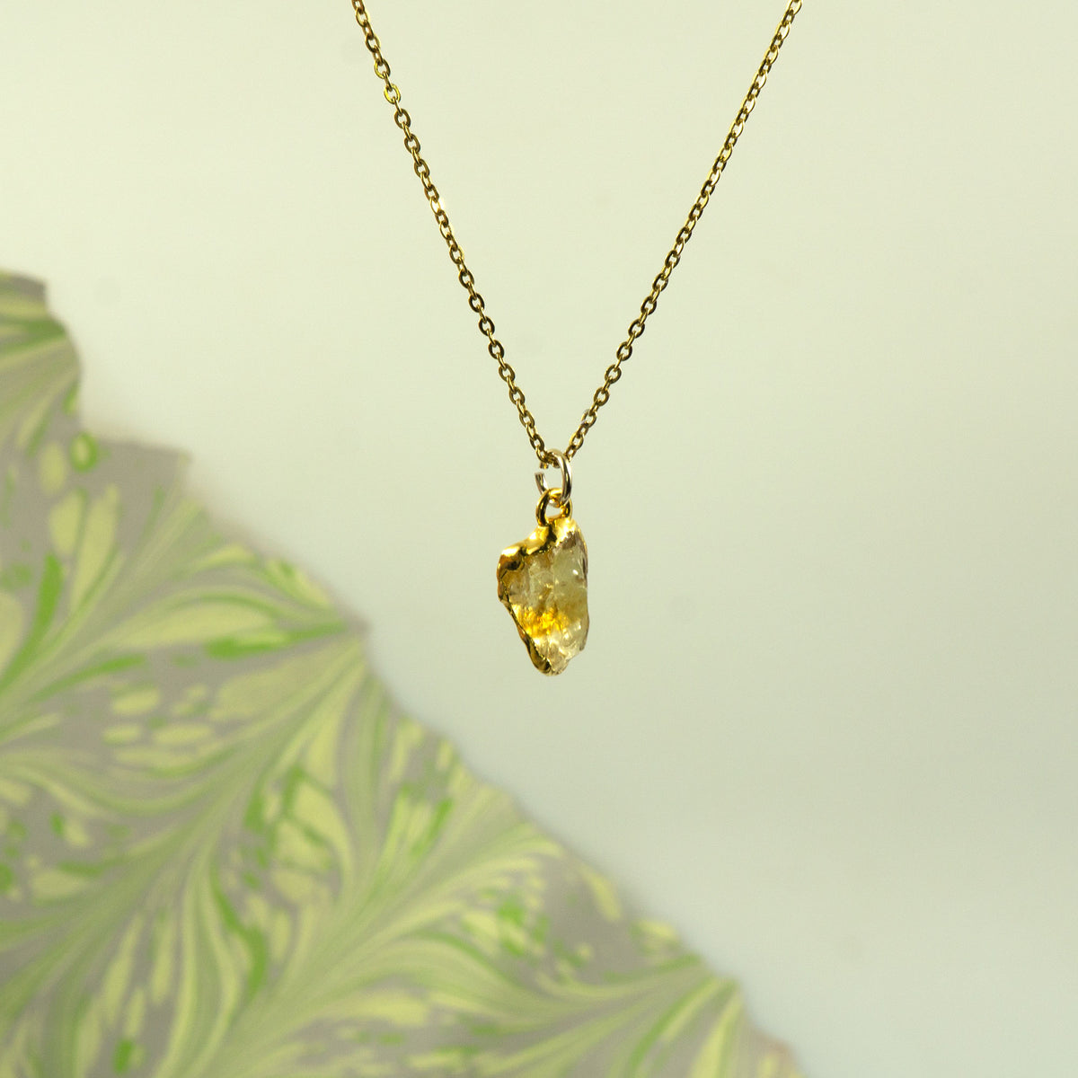 A gold chain necklace with a raw, irregular-cut yellow citrine gemstone pendant