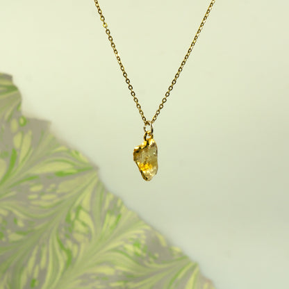 A gold chain necklace with a raw, irregular-cut yellow citrine gemstone pendant