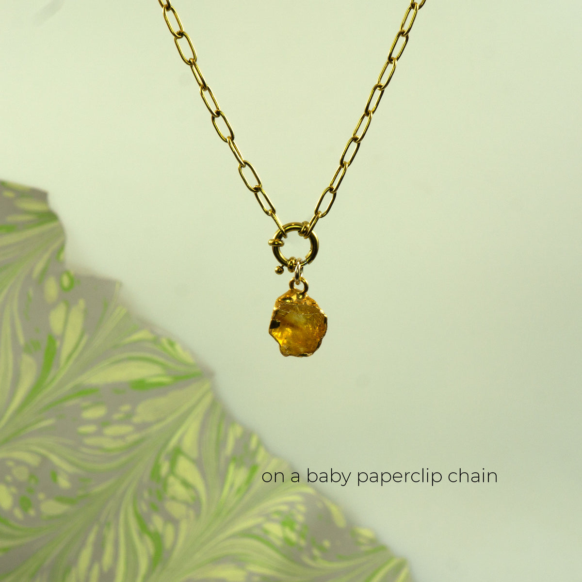 A gold paperclip chain necklace with a small gold ring clasp holding a faceted citrine yellow gemstone pendant