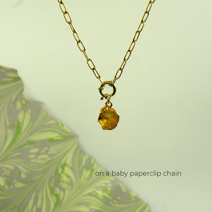 A gold paperclip chain necklace with a small gold ring clasp holding a faceted citrine yellow gemstone pendant