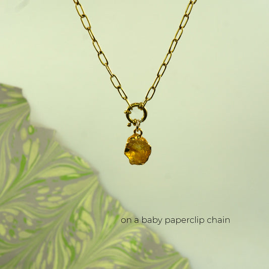 A gold paperclip chain necklace with a small gold ring clasp holding a faceted citrine yellow gemstone pendant