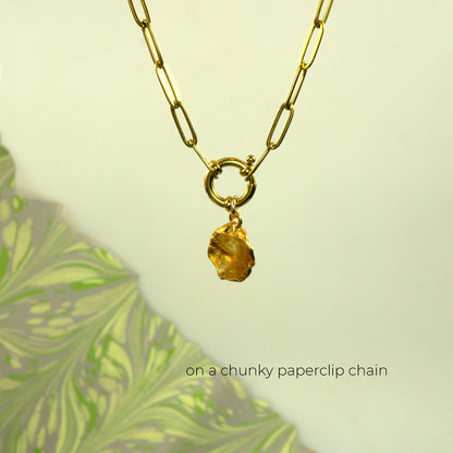 A gold paperclip chain necklace with a small ring clasp and a chunky, irregular faceted citrine amber-yellow gemstone pendant