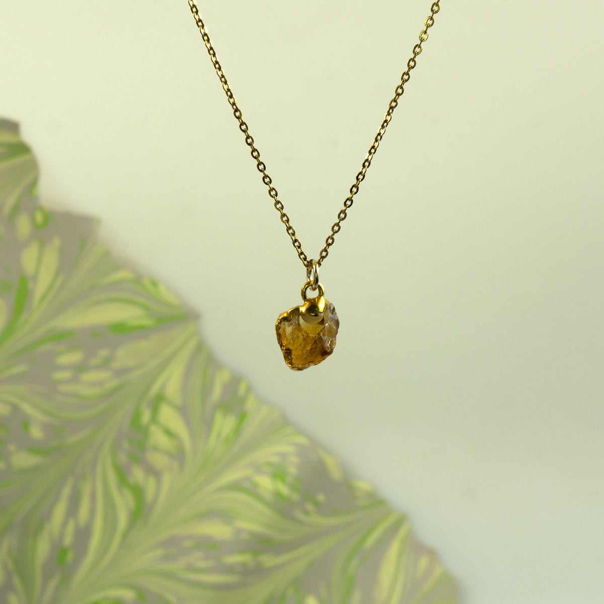 A gold chain necklace with a raw, irregular faceted amber-yellow citrine gemstone pendant