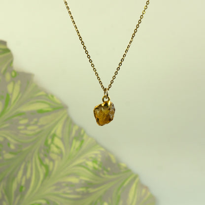 A gold chain necklace with a raw, irregular faceted amber-yellow citrine gemstone pendant