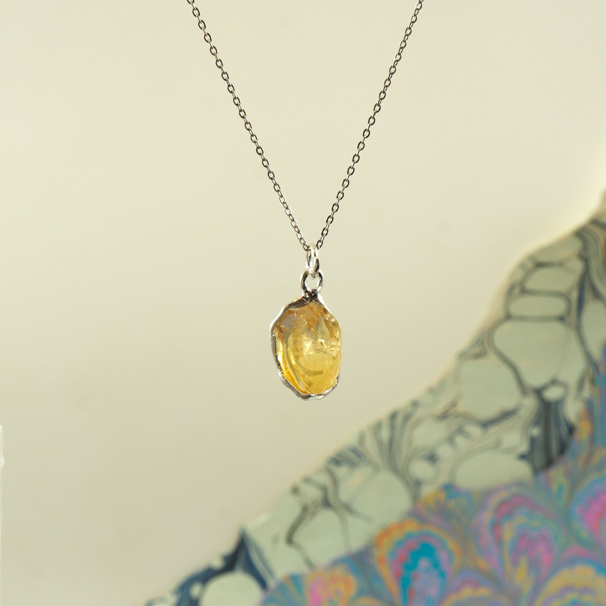 A silver chain necklace with a polished, irregular-shaped yellow citrine gemstone pendant