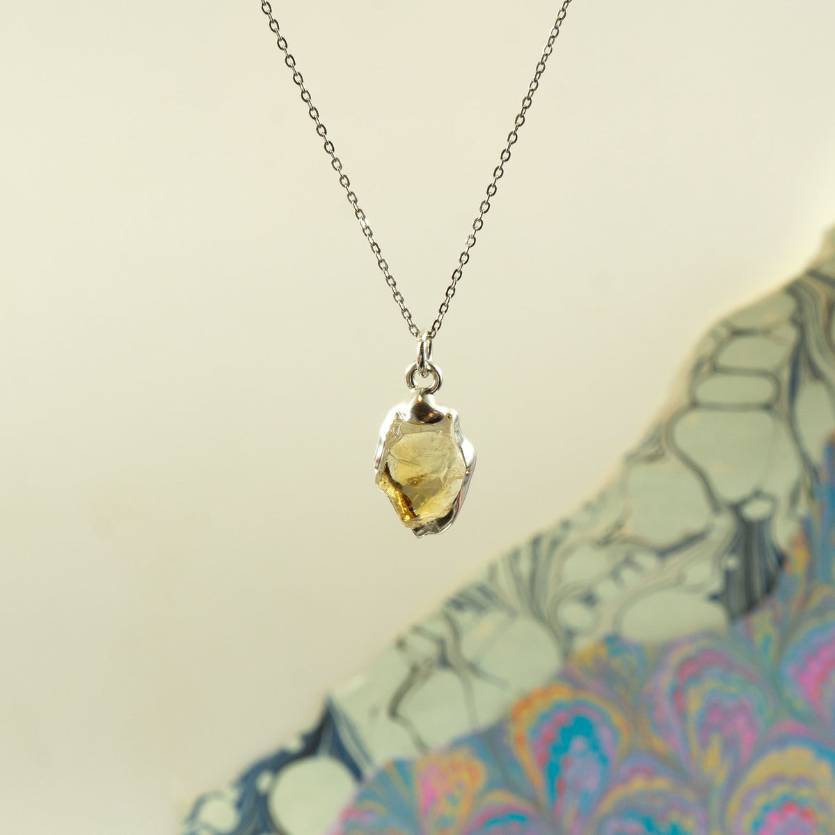 A silver chain necklace with a polished, irregular-shaped yellow citrine gemstone pendant