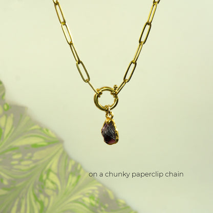 A gold paperclip chain necklace with a small ring connector and a teardrop-shaped dark purple garnet gemstone pendant