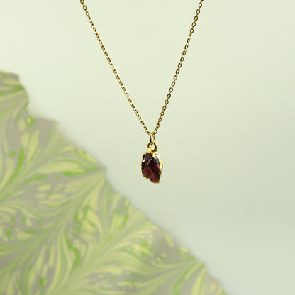 A gold chain necklace with a small, rough-cut dark red garnet gemstone pendant