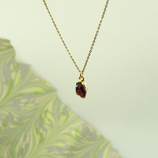 A gold chain necklace with a small, rough-cut dark red garnet gemstone pendant
