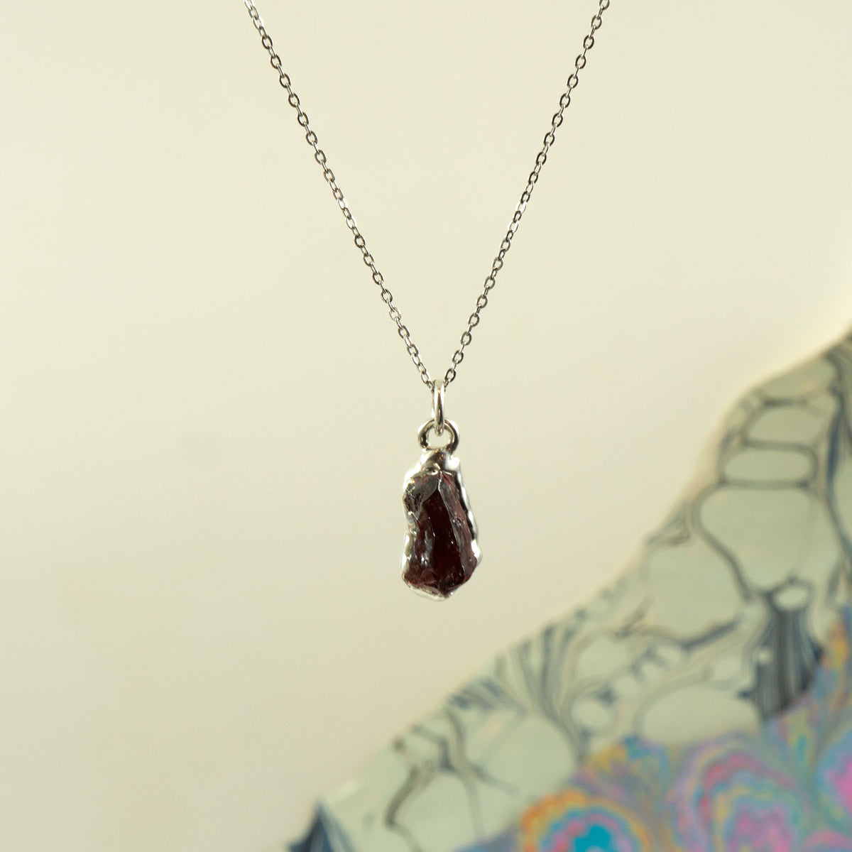 A silver chain necklace with a raw, irregular-cut dark red garnet gemstone pendant