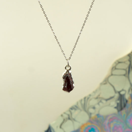 A silver chain necklace with a raw, irregular-cut dark red garnet gemstone pendant