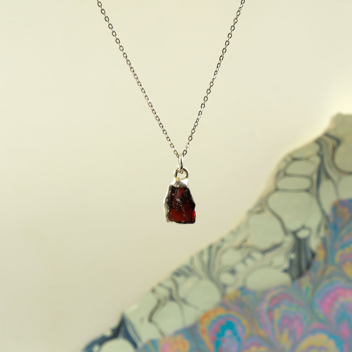 A silver chain necklace with a raw, irregular-cut dark red garnet-pendant gemstone pendant