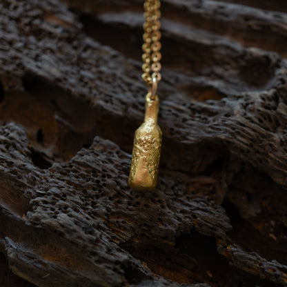 Gold bottle of beer pendant on a chain against a dark, textured background